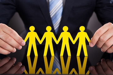 Businessman's Hands Holding Paper People Chain On Desk
