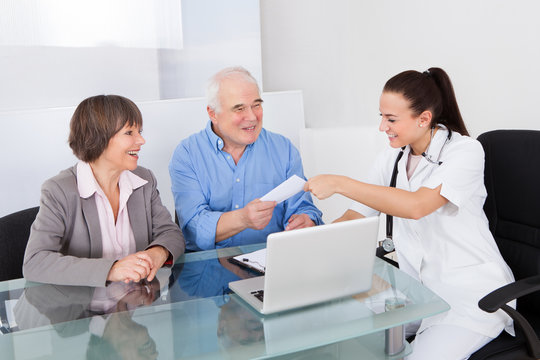 Doctor Giving Prescription To Senior Couple In Clinic