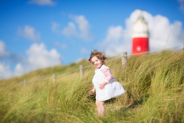 Cute toddler girl next to red lightshouse on a beach