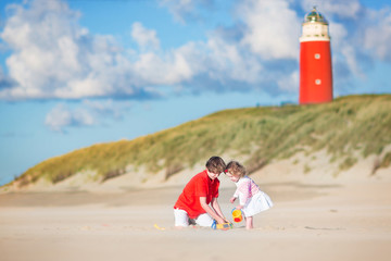 Happy brother and his sister playing on beach next to lighthouse
