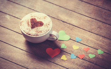Cup with coffee and heart shape papers on wooden table.