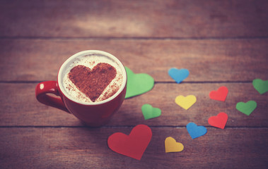 Cup with coffee and heart shape papers on wooden table.