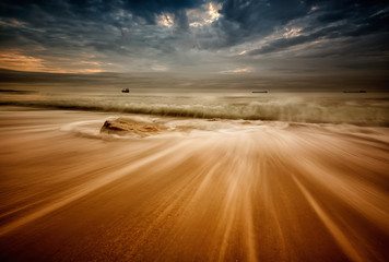 Fototapeta premium Stormy sea beach with slow shutter and waves flowing out