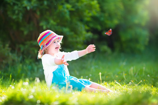 Pretty toddler girl playing with butterfly in garden