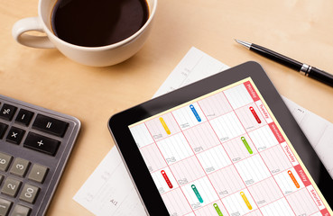 Tablet pc showing calendar on screen with a cup of coffee on a d