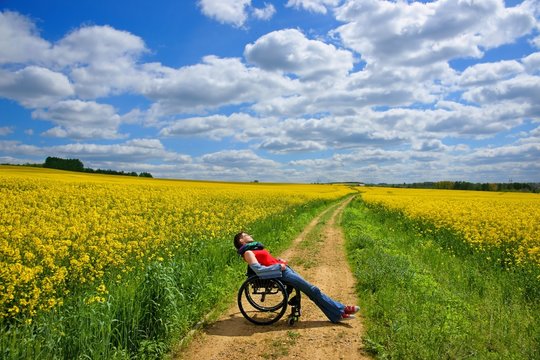 Disabled woman sunbathing on a wheelchair, rape field, spring
