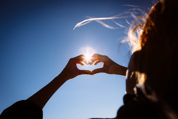 Hands making love shape sign on bright blue sky.