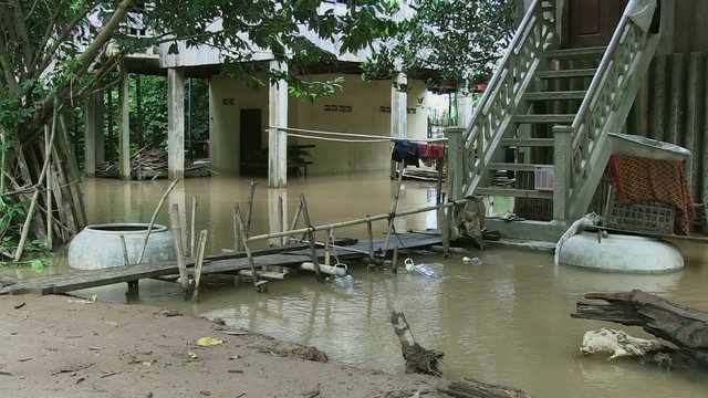 Flood waters under stilt-houses and makeshift access footbridge in the foreground