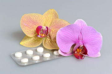 Two orchid flowers with film-coated tablets on gray