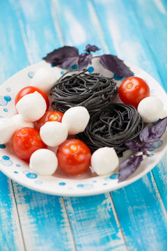 Plate with tomatoes, mozzarella, black tagliatelle and basil