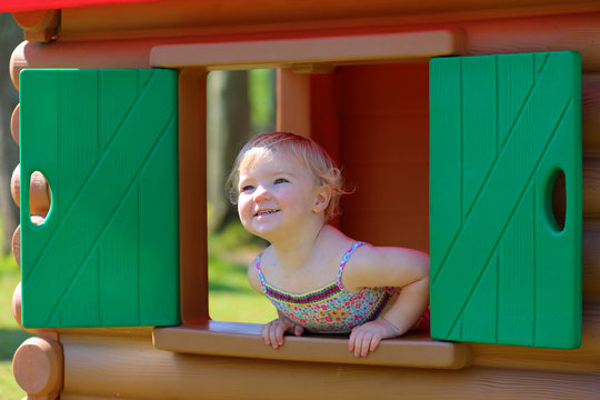 Little girl having fun outdoors hiding in plastic playhouse