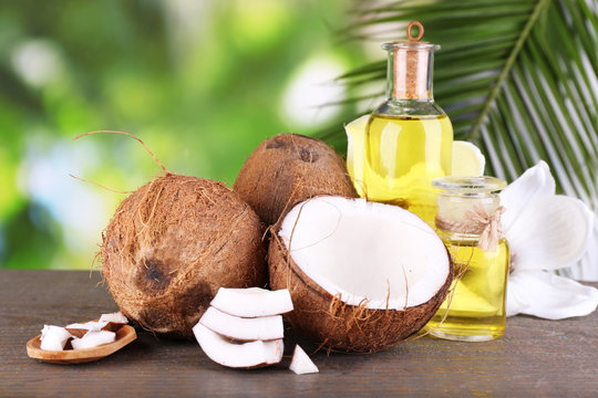 Coconuts and coconut oil on wooden table, on nature background