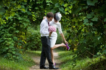 Naklejka na ściany i meble Groom and bride in a botanical garden. Bride adjusts her shoes.