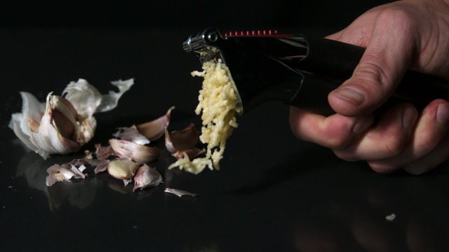 Hand using garlic press on black background
