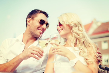 smiling couple in sunglasses drinking wine in cafe