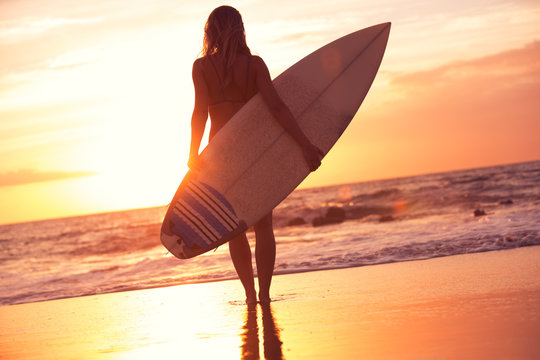 Silhouette surfer girl on the beach at sunset
