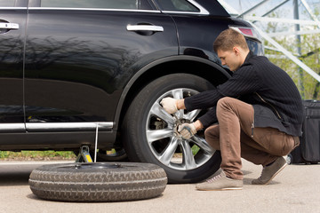 Young man changing the punctured tyre on his car