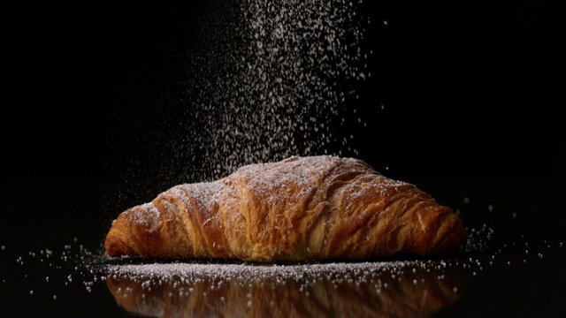 Powdered sugar sprinkling onto a croissant