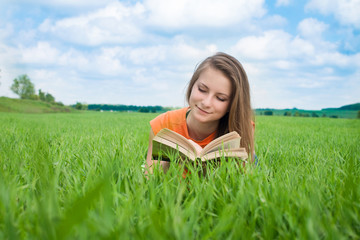 Naklejka na ściany i meble Beautiful young woman - student reading book in the meadow.
