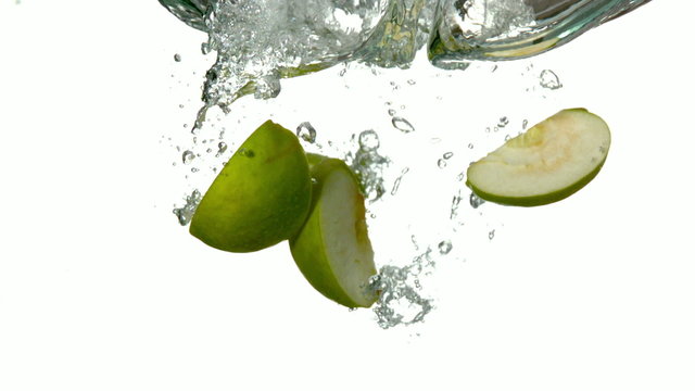 Apple segments plunging into water on white background