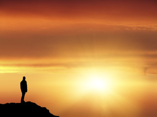Man silhouette on top of a mountain looking the horizon concept of success 
