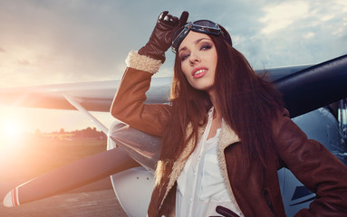 Portrait of young beautiful woman pilot in front of airplane.