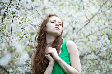 Beautiful young girl standing near blooming trees in spring gard