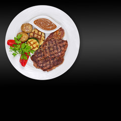 Grilled steak, potatoes and vegetables on black background.