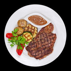 Grilled steak, potatoes and vegetables on black background.