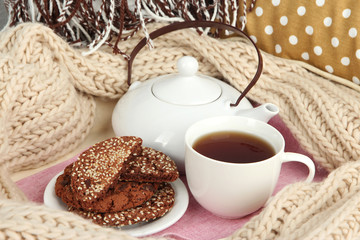 Cup and teapot with cookies on tray and scarf on bed close up