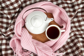 Cup and teapot on wooden stand and scarf on fabric background