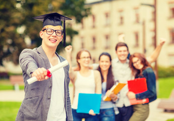 smiling teenage boy in corner-cap with diploma