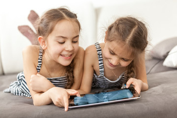 portrait of two smiling girls lying on couch and using tablet