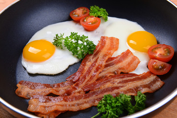 Scrambled eggs and bacon on frying pan on table close-up