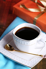 Cup of coffee and gift on wooden table close-up