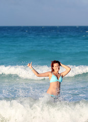 Smiling young redhead woman standing in the ocean wave