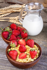 cornflakes in a wooden bowl with milk and strawberries
