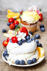 Meringue cake decorated with fresh fruits, standing on wood