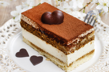 Tiramisu cake on white plate. Blossom apple branch in the back