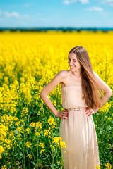 Fototapeta premium Beautiful happy girl standing on the colza field.