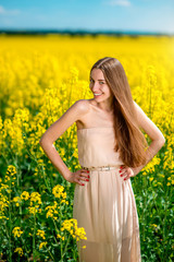Fototapeta premium Beautiful happy girl standing on the colza field.