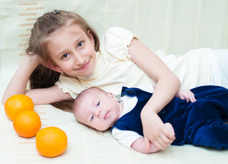 Older sister hugging baby lying on the bed with oranges