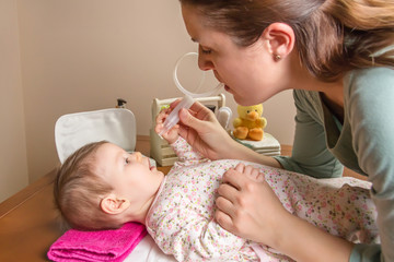 Mother cleaning mucus of baby with nasal aspirator