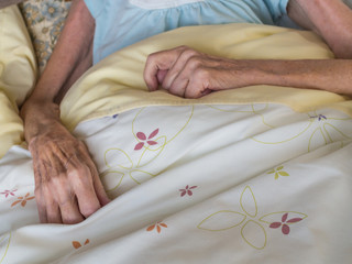 Old woman with very skinny arms and hands lying in a bed