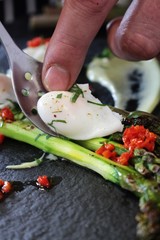 chef preparing poached quail eggs on asparagus