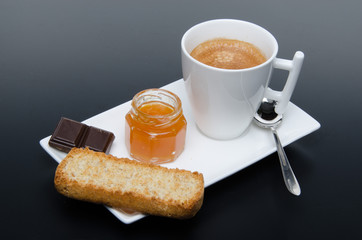 A cup of coffee with chocolate, jam and  a rusk
