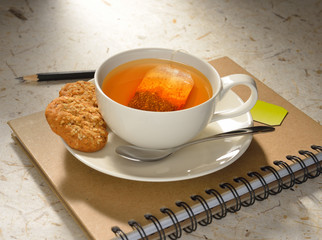 Cup of tea with tea bag and cookies on notebook