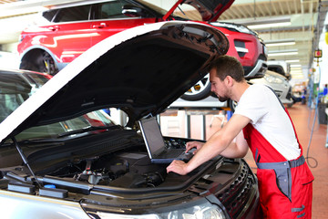 KFZ Mechaniker mit Diagnosegerät am Motor eines Fahrzeuges