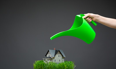 Close up of watering pot pouring home model with green grass 