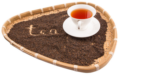 A cup of tea in a wicker tray with written TEA word on dried tea